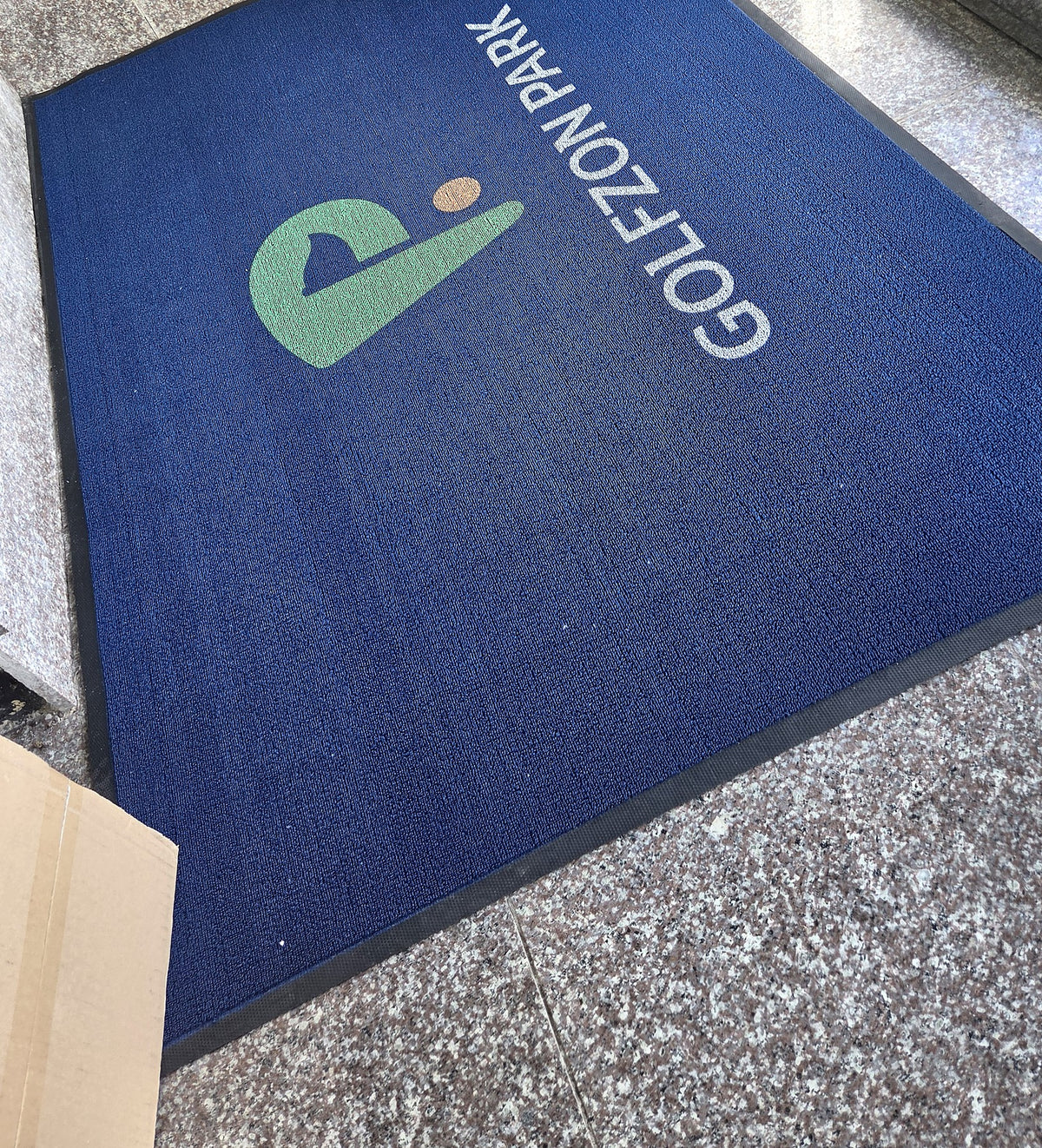 Loop 7 mm custom logo mat in navy blue with a green and white logo at a doorway, customer photo