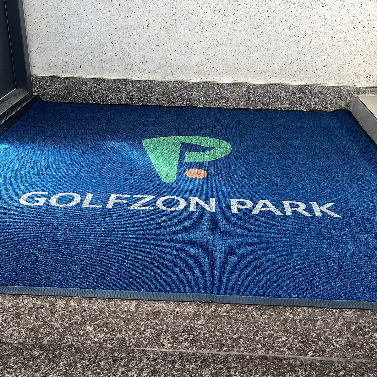 Loop 7 mm custom logo mat in royal blue with a white and green logo, installed at a store entrance, customer photo